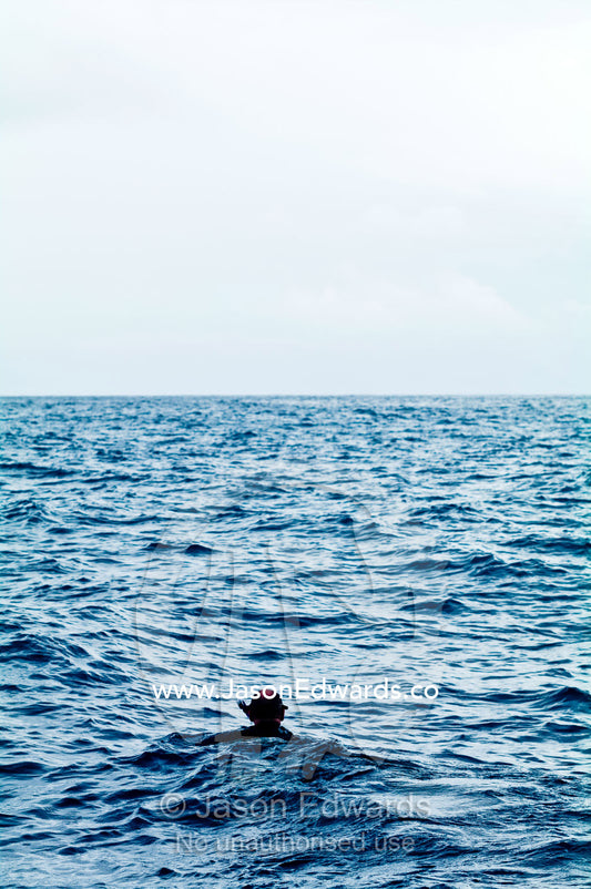 A lone snorkeler swims across the surface of a wide ocean. Vava'u Island Group, Pacific Ocean, Oceania, Kingdom of Tonga.