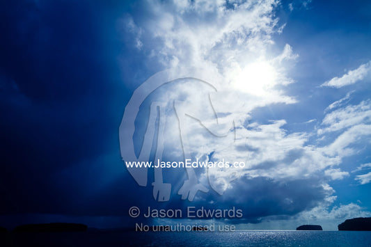 Sun rays pierce an immense storm descending over tropical islands. Vava'u Island Group, Pacific Ocean, Oceania, Kingdom of Tonga.