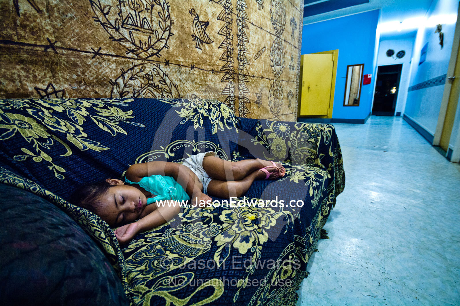 A small girl sleeps on a couch in the foyer of a backpackers' lodge. Vava'u Island Group, Pacific Ocean, Oceania, Kingdom of Tonga.