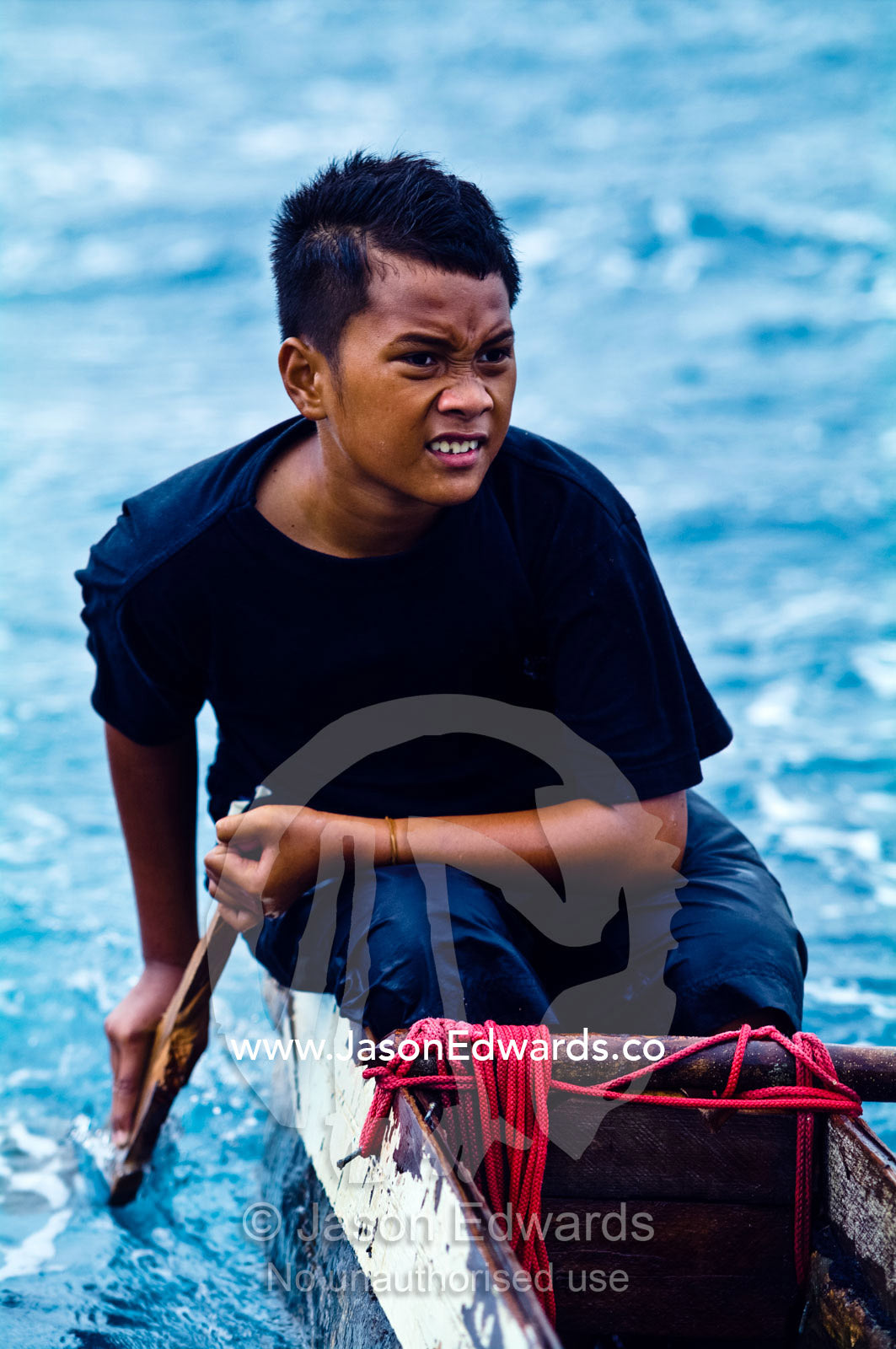 A young boy steers his outrigger canoe as it is towed through a storm. Vava'u Island Group, Pacific Ocean, Oceania, Kingdom of Tonga.