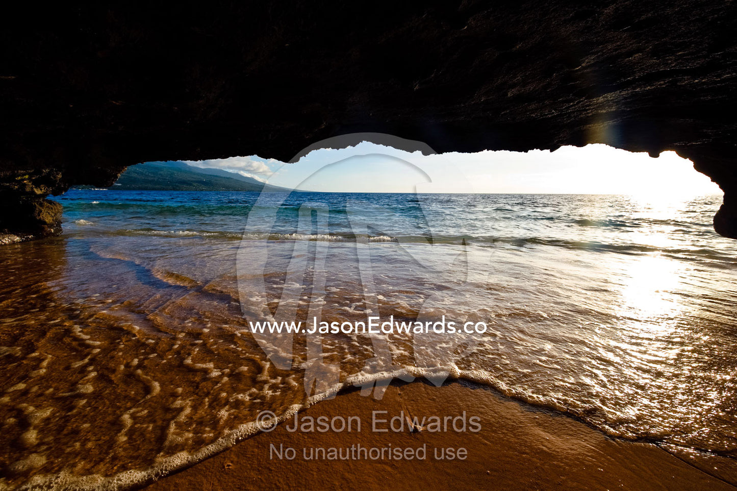 The lip of a foamy wave laps a sandy beach inside an ocean cave. Rainbow Reef, Taveuni Island, Pacific Ocean, Fiji Islands.
