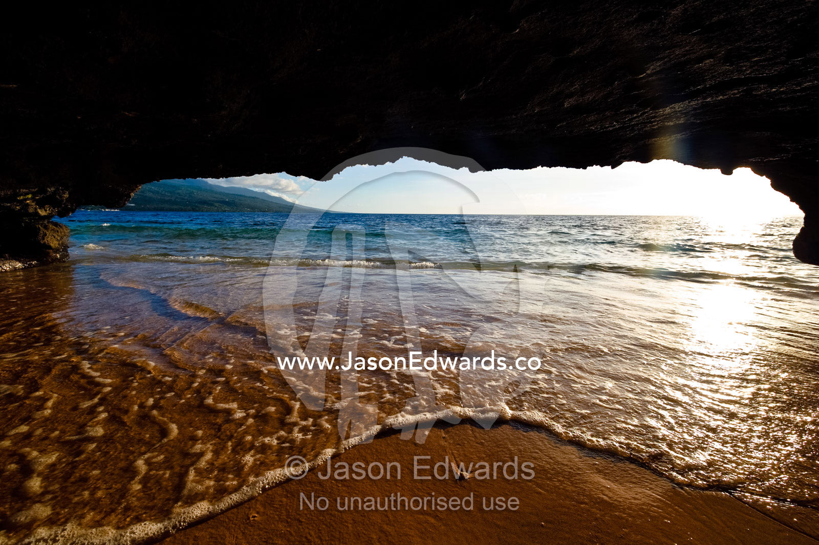 The lip of a foamy wave laps a sandy beach inside an ocean cave. Rainbow Reef, Taveuni Island, Pacific Ocean, Fiji Islands.