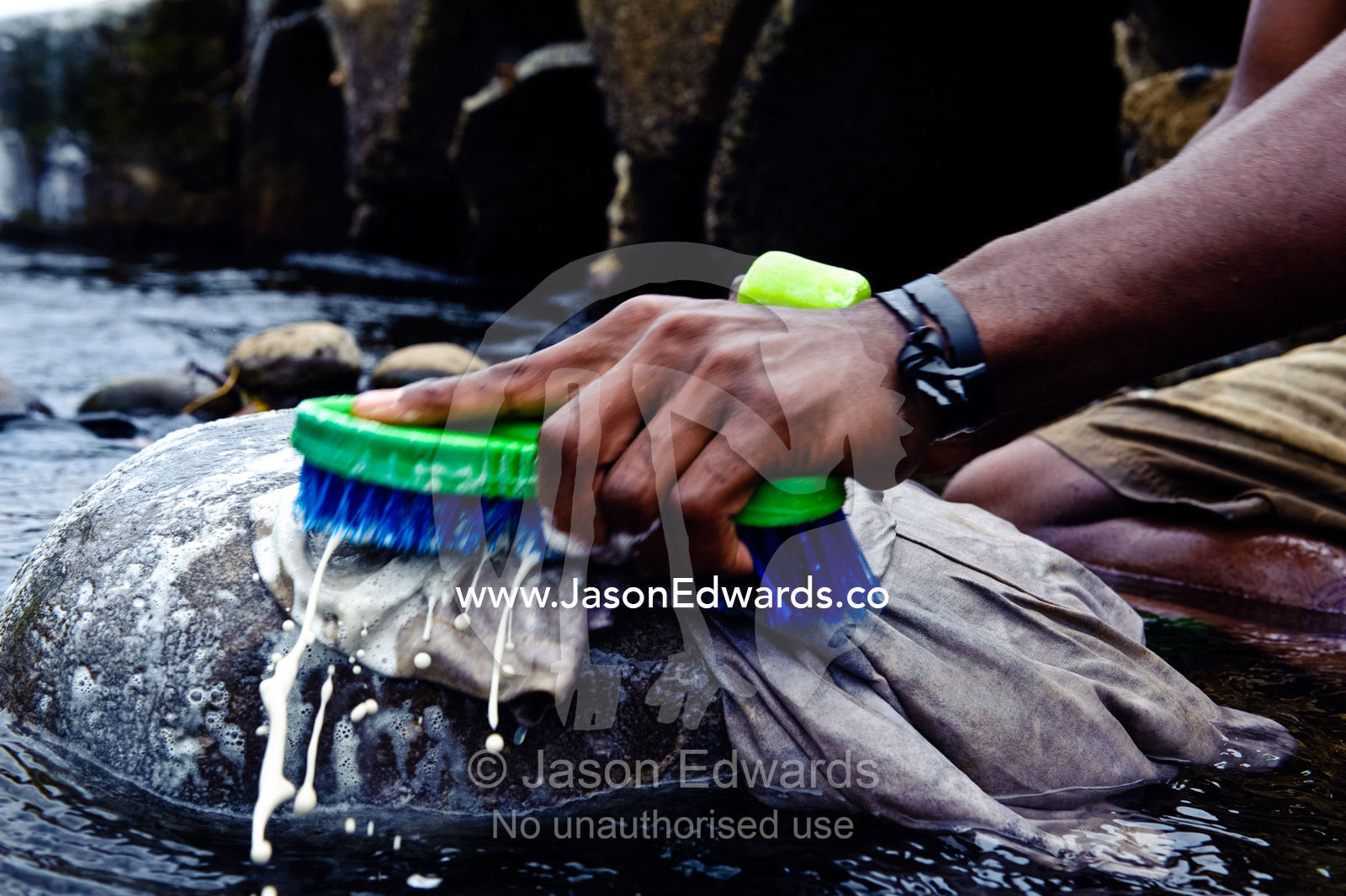 Washing clothes against a river rock using a scrubbing brush and soap. Taveuni Island, Pacific Ocean, Fiji Islands.