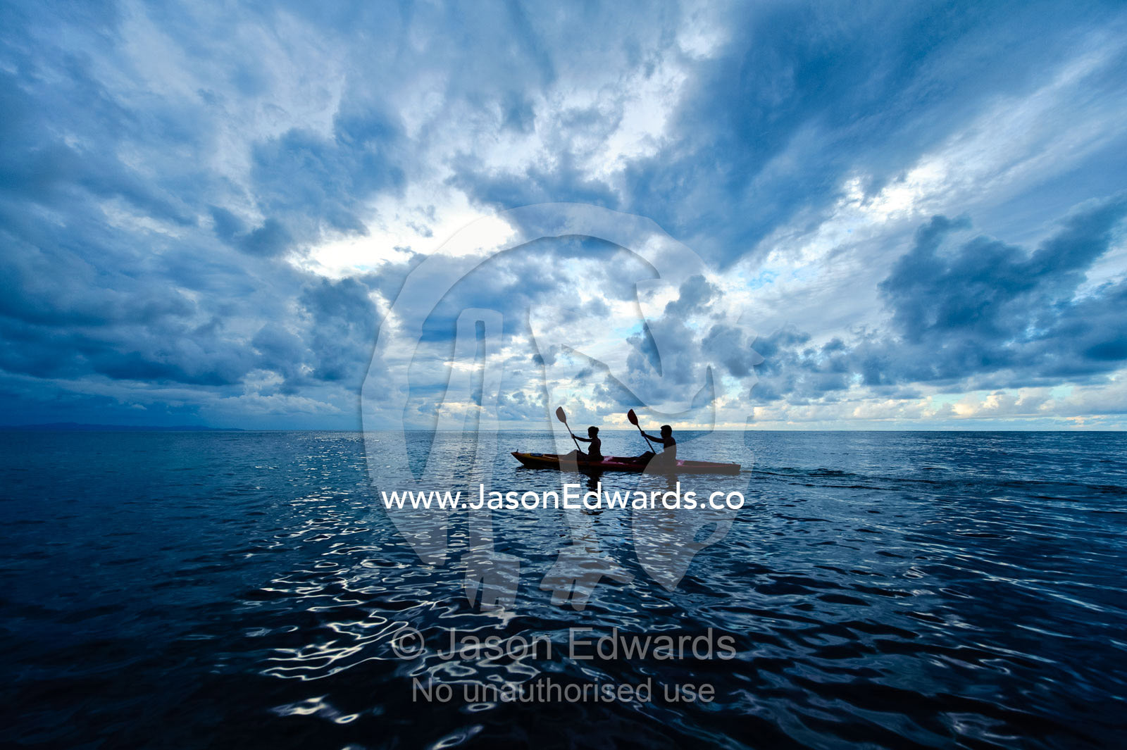 A couple paddles a sea kayak across a calm ocean beneath a storm. Cobia Island, Ringgold Atolls, Pacific Ocean, Fiji Islands.