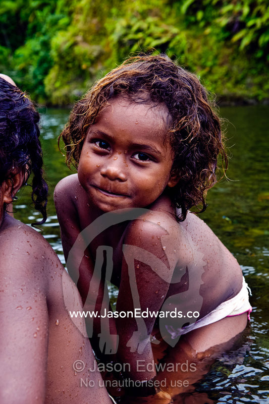 A cheeky girl with messy hair bathing in a small forest river. Taveuni Island, Pacific Ocean, Fiji Islands.