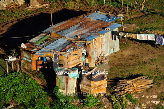 A farming family waves from their corrugated tin home to a balloon. Viti Levu, Pacific Ocean, Fiji Islands.