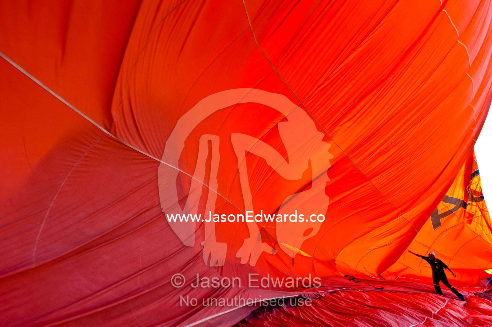 A crewman assists a hot air balloon deflate like a giant orange wave. Viti Levu, Pacific Ocean, Fiji Islands.