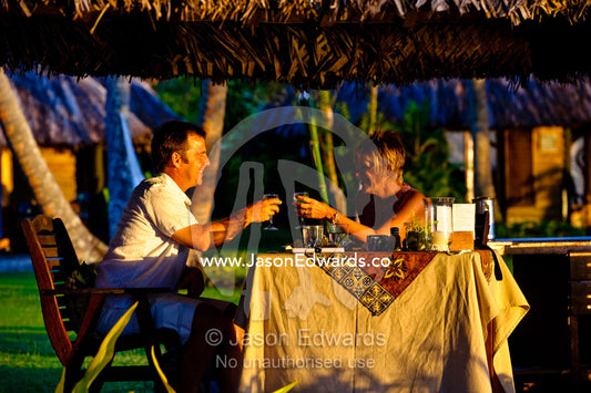 A couple toast each other over a sunset dinner on a tropical island. Paradise Taveuni, Taveuni Island, Pacific Ocean, Fiji Islands.