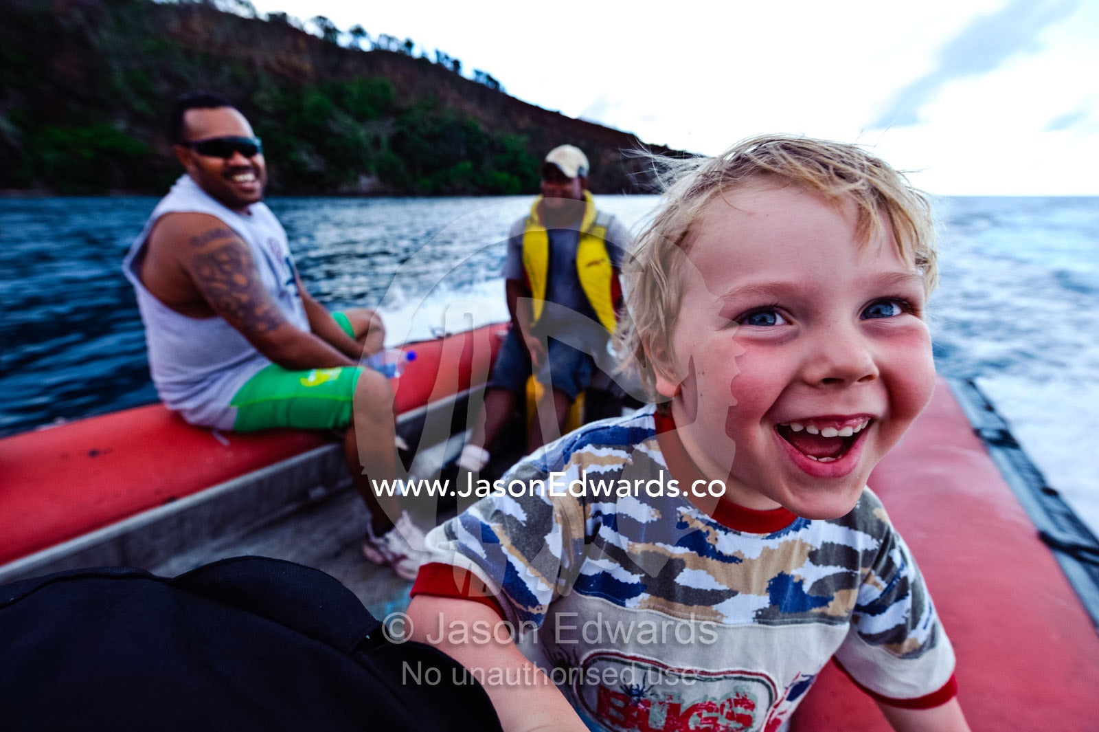 A boy laughing as he speeds around a lagoon in a zodiac boat. Cobia Crater, Cobia Island, Ringgold Atolls, Pacific Ocean, Fiji Islands.