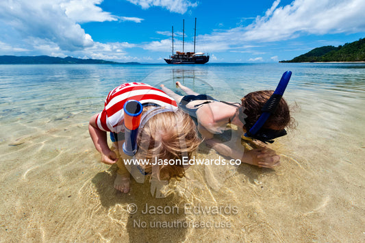 A mother and son search the sand for sea creatures with snorkels. Rabi Island, Somosomo Strait, Pacific Ocean, Fiji Islands.