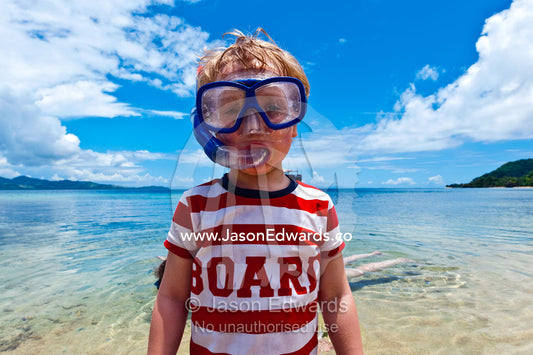 A boy wears his snorkel and mask in the shallows of a tropical island. Rabi Island, Somosomo Strait, Pacific Ocean, Fiji Islands.