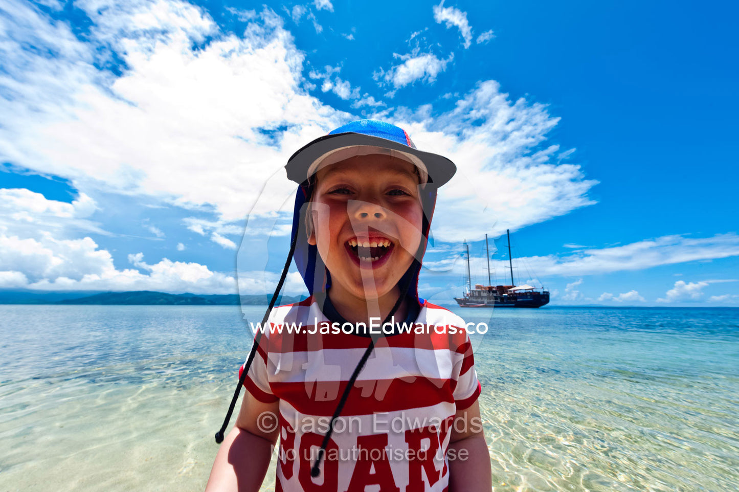 A laughing boy stands in the warm shallows of a tropical island. Rabi Island, Somosomo Strait, Pacific Ocean, Fiji Islands.