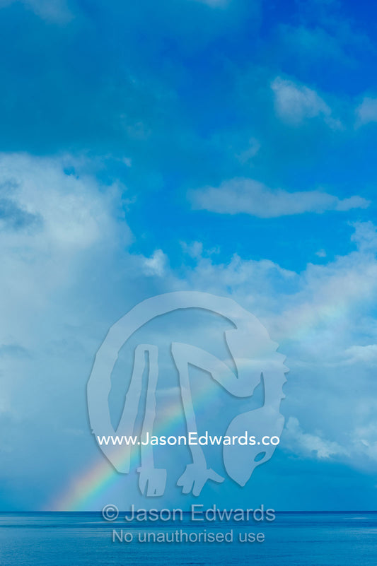 A rainbow on the horizon touches the surface of a calm tropical ocean. Taveuni Island, Somosomo Strait, Pacific Ocean, Fiji Islands.