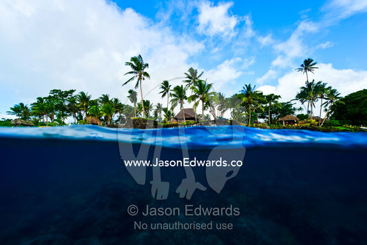 A coral reef lines the shore beneath a tropical island resort. Home Reef, Taveuni Island, Somosomo Strait, Pacific Ocean, Fiji Islands.
