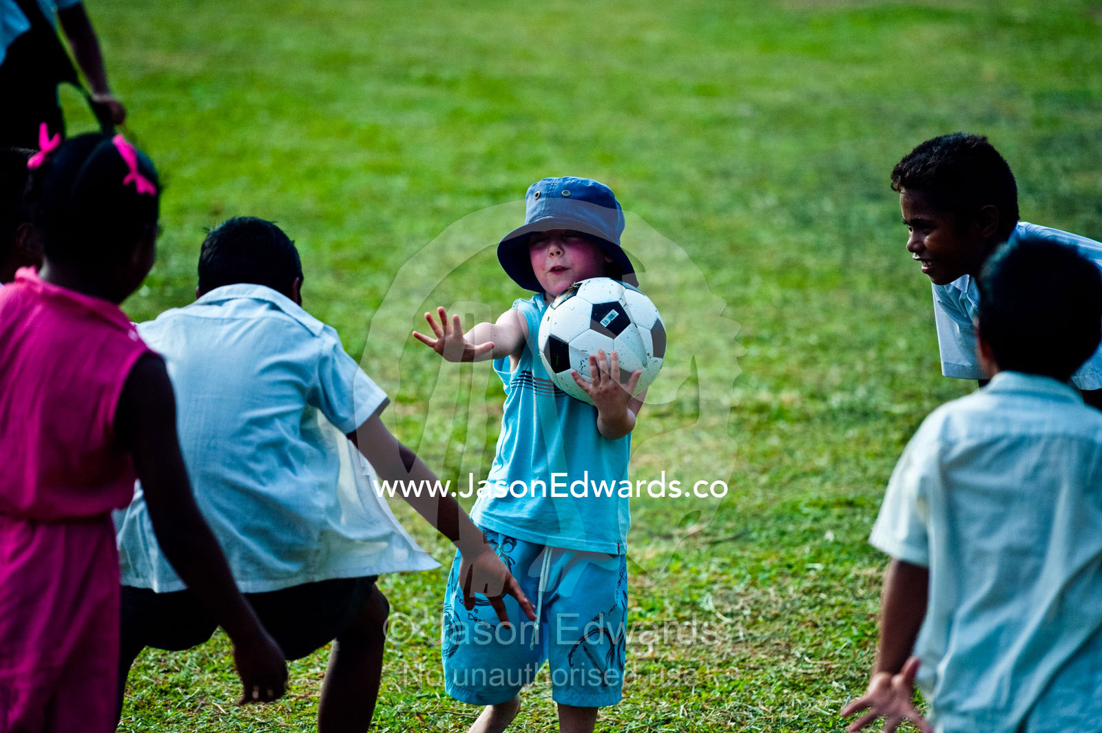 A young tourist plays with a football with village school children. Tabiang Village, Rabi Island, Somosomo Strait, Pacific Ocean, Fiji Islands.