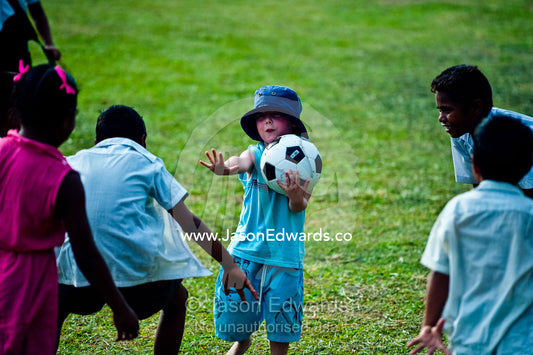 A young tourist plays with a football with village school children. Tabiang Village, Rabi Island, Somosomo Strait, Pacific Ocean, Fiji Islands.