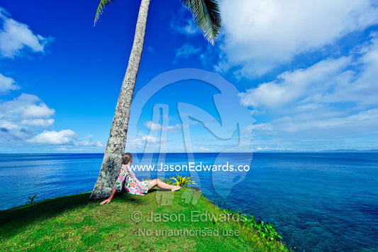 A woman relaxes under a palm tree on an idyllic tropical island. Taveuni Island, Somosomo Strait, Pacific Ocean, Fiji Islands.