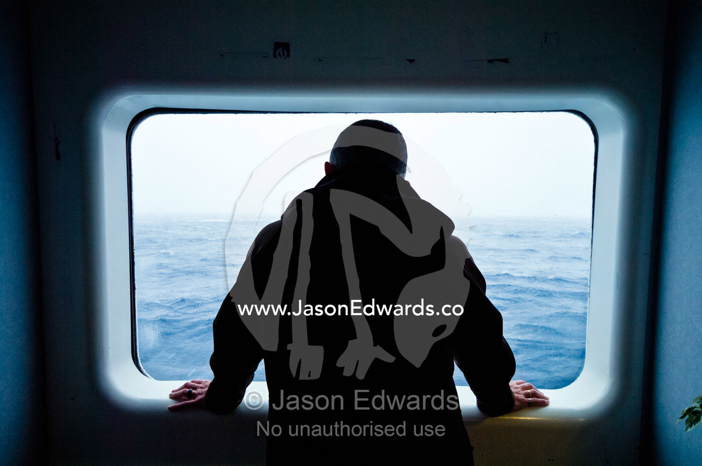 A tourist watches a stormy South Ocean from a warm ships window. The Drake Passage between the Atlantic Ocean and Pacific Ocean, Argentina, Antarctica.