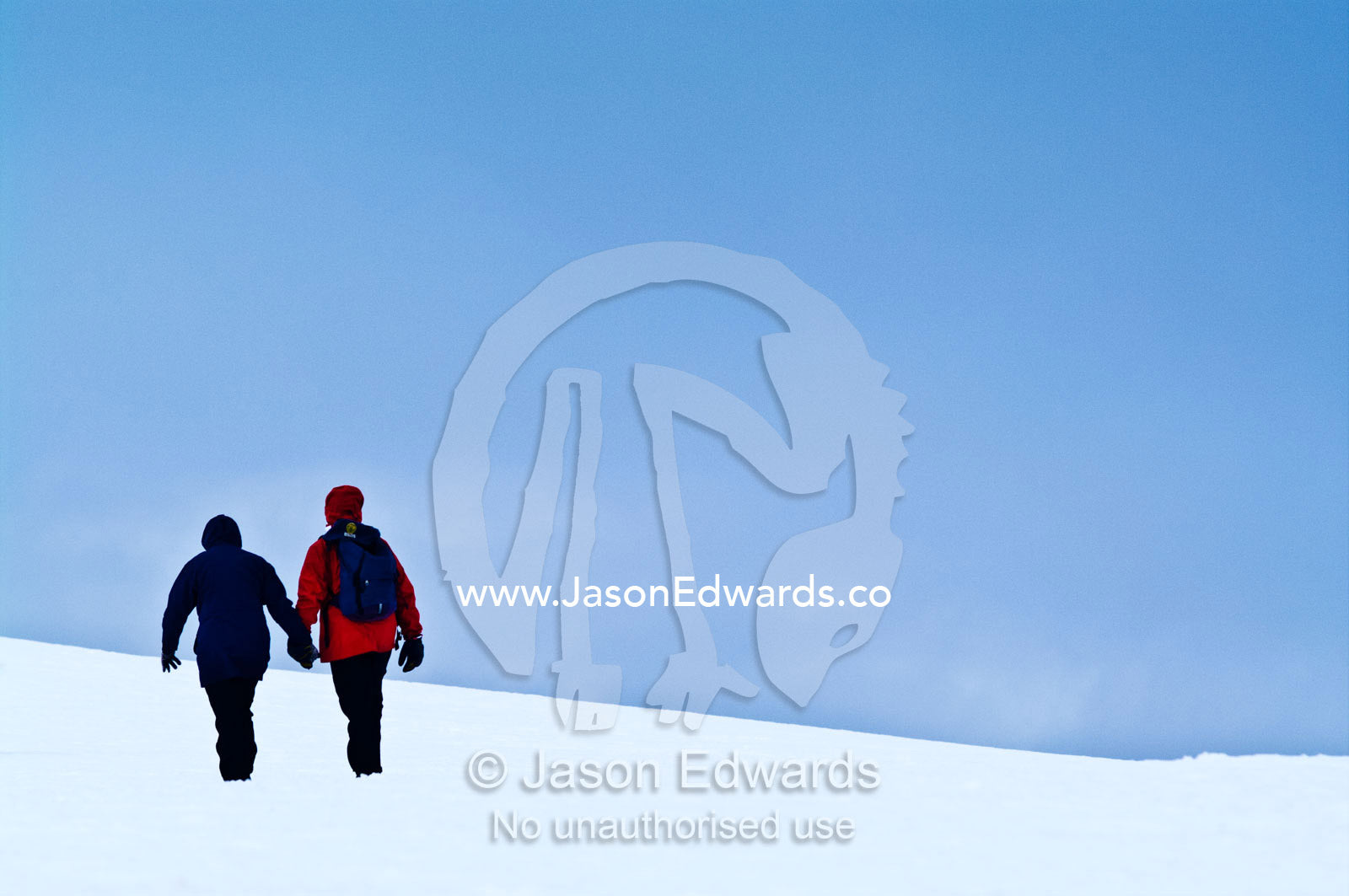 A tourist couple explore a barren ice slope on a rugged island. Prospect Point, Crystal Sound, Antarctic Peninsula, Antarctic Circle, Antarctica.