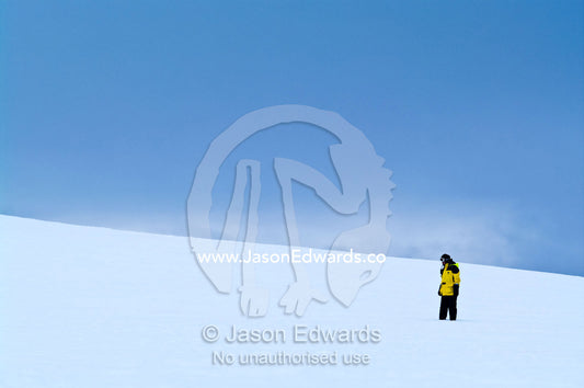 An expedition guide explores a barren ice slope on a rugged island. Prospect Point, Crystal Sound, Antarctic Peninsula, Antarctic Circle, Antarctica.