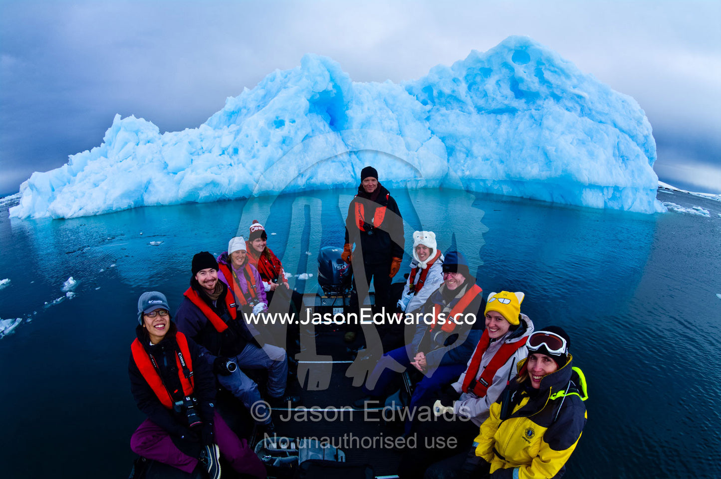 Tourists in a boat pose in front of a jagged blue Antarctic iceberg. Fish Islands, Flounder Island, The Minnows, Crystal Sound, Antarctic Peninsula, Antarctic Circle, Antarctica.