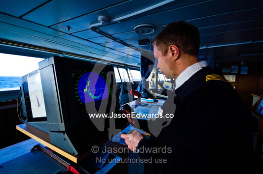 An officer on duty aboard a ship's bridge examines a radar screen. Drake Passage, Atlantic Ocean, Pacific Ocean, Antarctica.