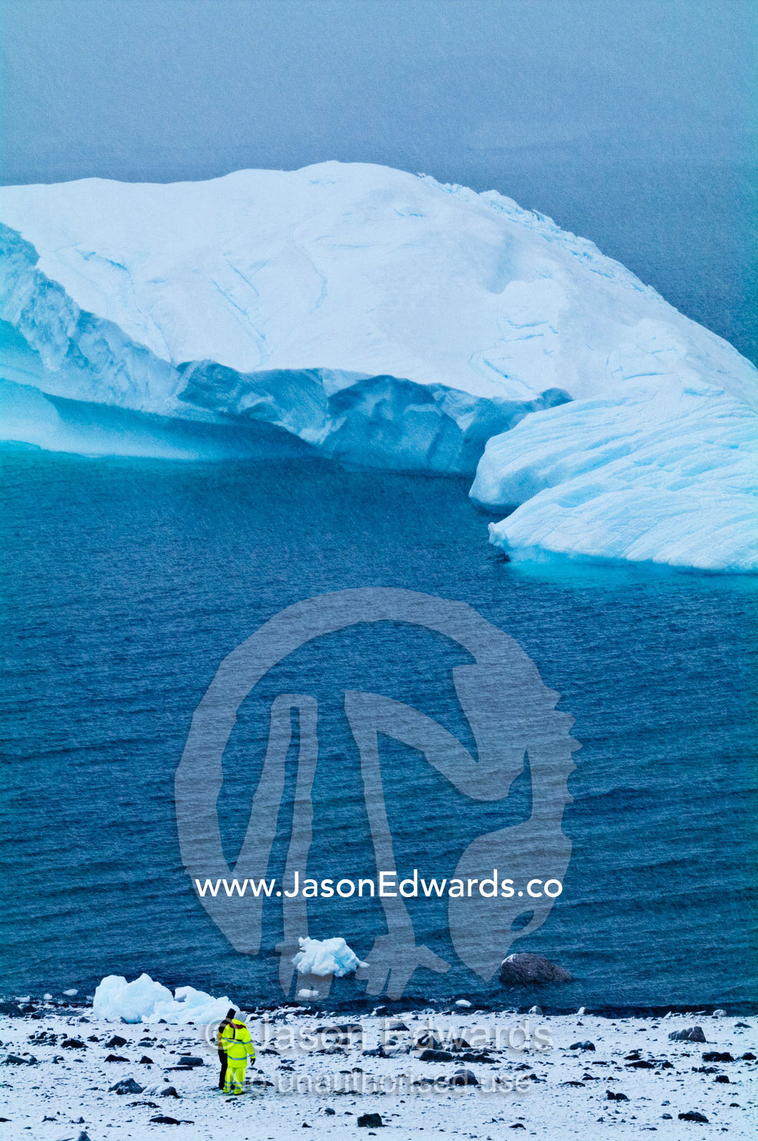 A tourist in fluorescent clothing watches an iceberg near the shore. Danco Island, Antarctic Peninsula, Antarctica.
