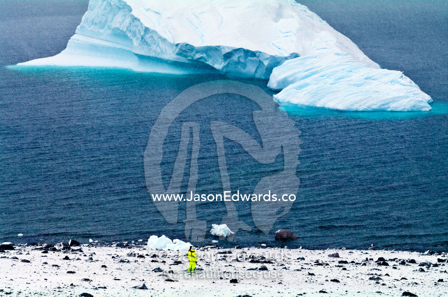 A tourist in fluorescent clothing watches an iceberg near the shore. Danco Island, Antarctic Peninsula, Antarctica.