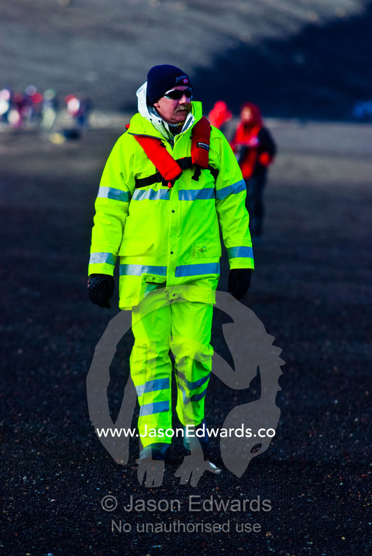 A tourist in fluorescent alpine clothing hiking on a volcanic beach. Whalers Bay, Antarctic Historic Site, Port Foster, Deception Island, South Shetland Islands, Antarctic Peninsula, Antarctica.
