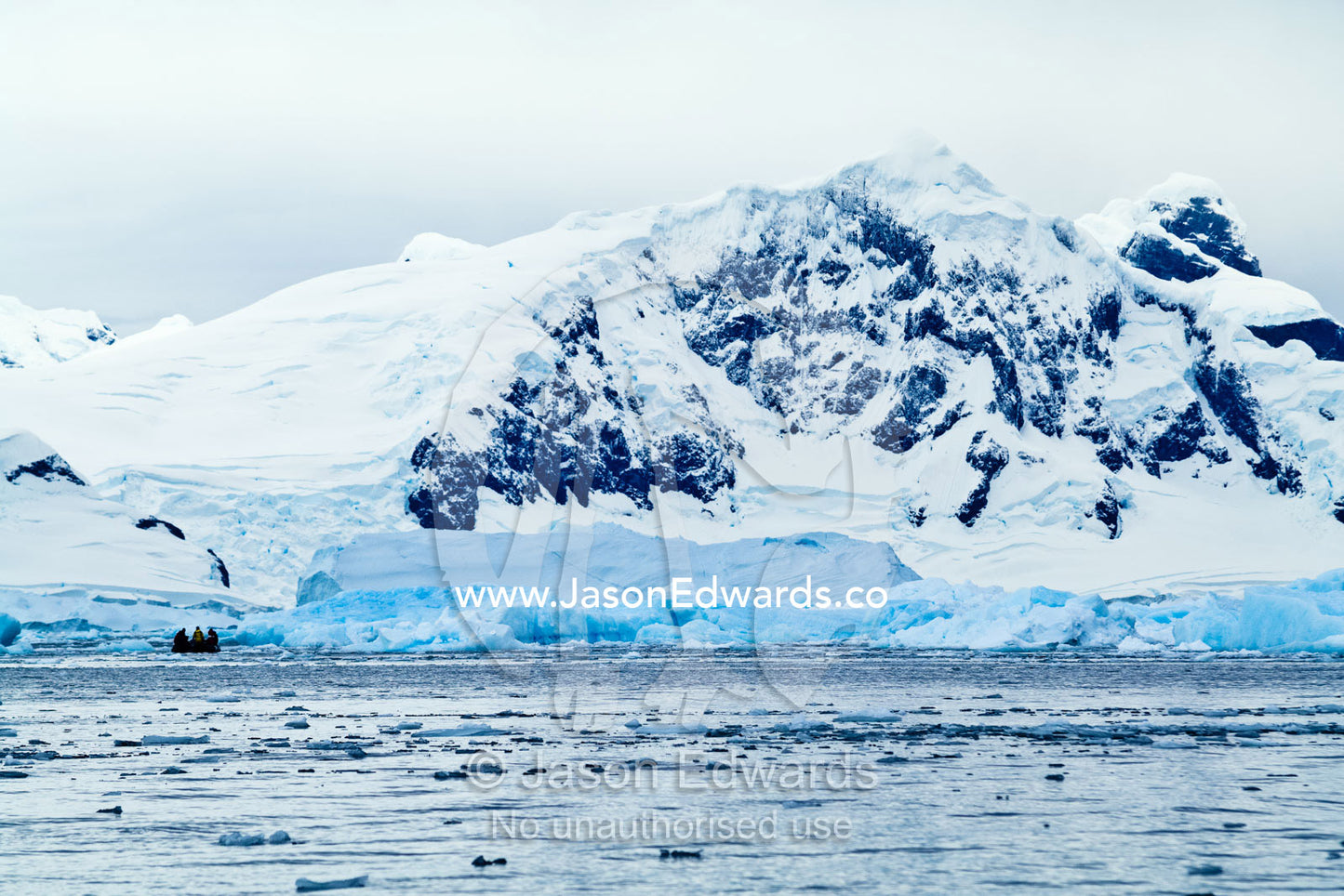 Tourists explore an icy bay beneath snowy peaks in an inflatable boat. Fish Islands, Flounder Island, The Minnows, Crystal Sound, Antarctic Peninsula, Antarctic Circle, Antarctica.