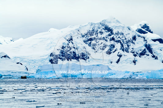 Tourists explore an icy bay beneath snowy peaks in an inflatable boat. Fish Islands, Flounder Island, The Minnows, Crystal Sound, Antarctic Peninsula, Antarctic Circle, Antarctica.
