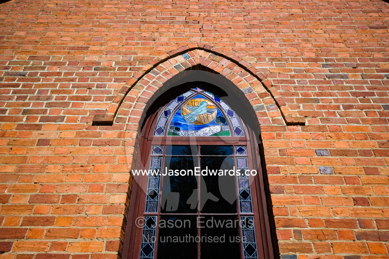 A stain glass window in a small country church made of red bricks. Elphinstone, Victoria, Australia.