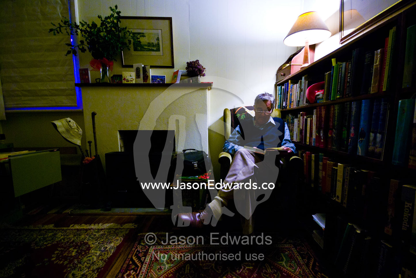 An elderly man reading a book by lamplight in his country home. Castlemaine, Victoria, Australia.