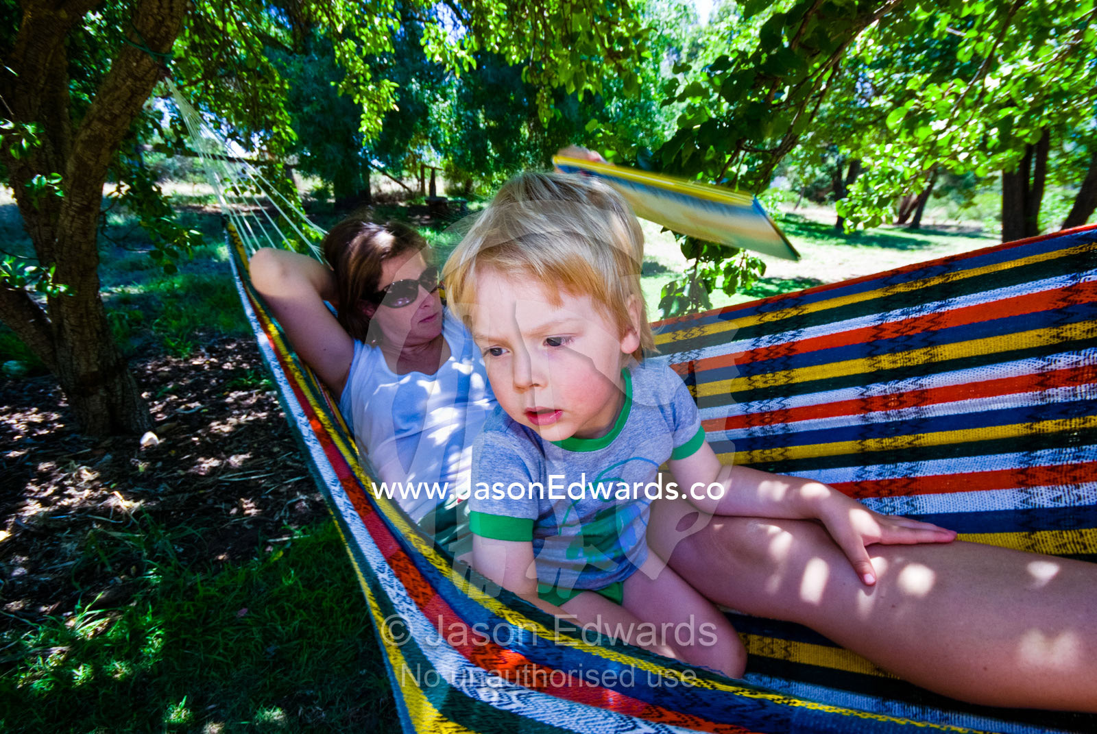 Mother and son swing in a hammock under fruit trees on a summers day. Castlemaine, Victoria, Australia.