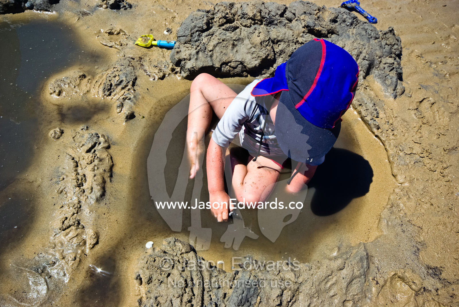 A boy plays with his toys in a sandy, muddy puddle on a summer beach. Rye Beach, Melbourne, Victoria, Australia.
