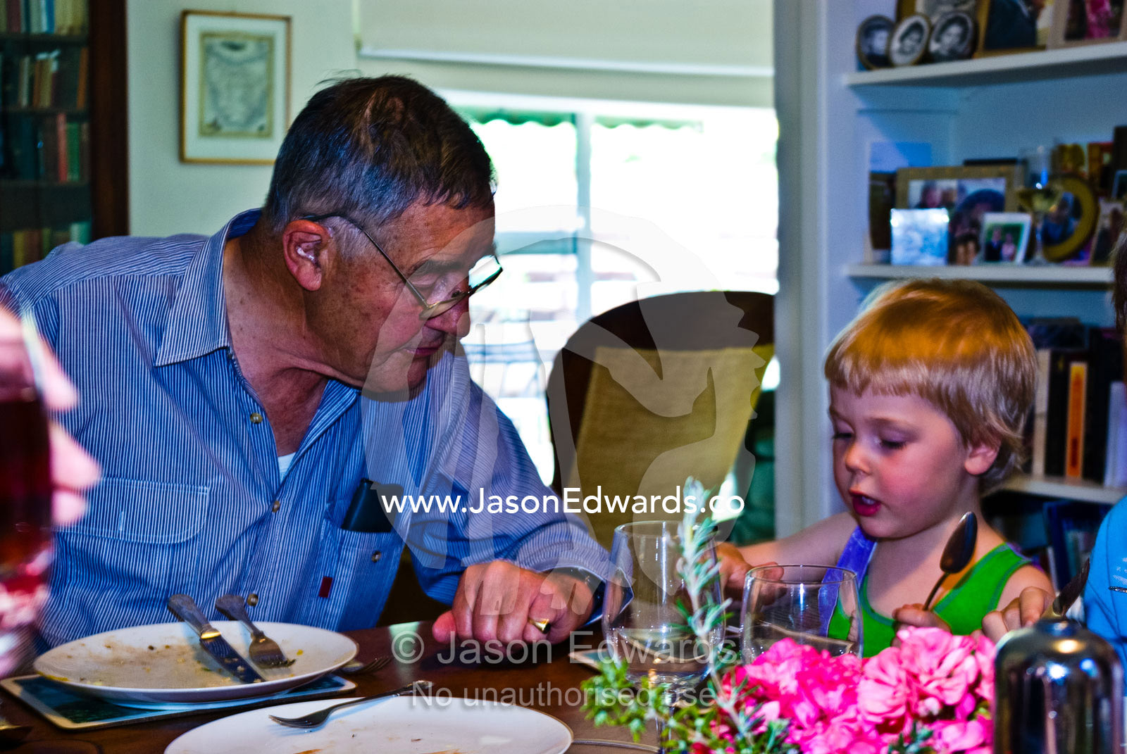 A grandfather listens intently to his grandson talking over dinner. East Malvern, Melbourne, Victoria, Australia.
