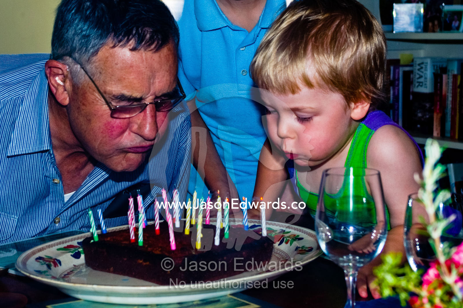 A grandson helps his grandfather blow out candles on a birthday cake. East Malvern, Melbourne, Victoria, Australia.