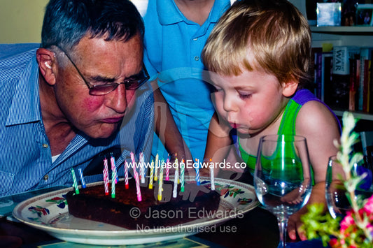 A grandson helps his grandfather blow out candles on a birthday cake. East Malvern, Melbourne, Victoria, Australia.