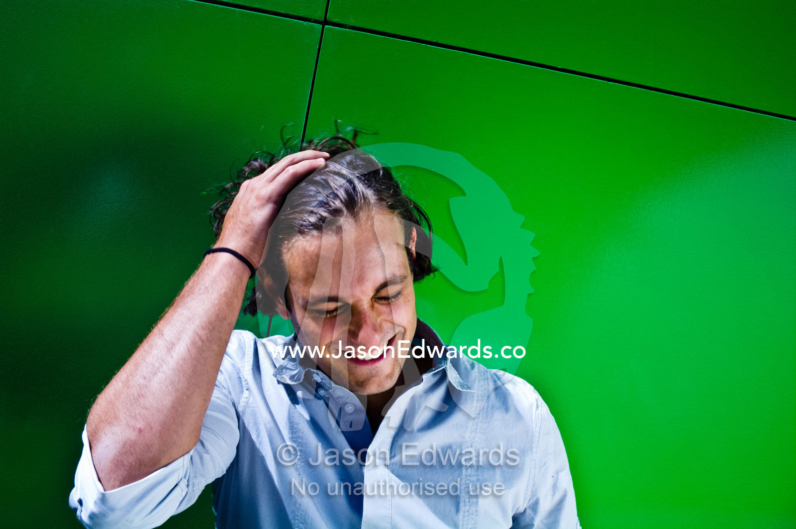 An attractive young man flicks back his hair resting against a wall. Carlton, Melbourne, Victoria, Australia.