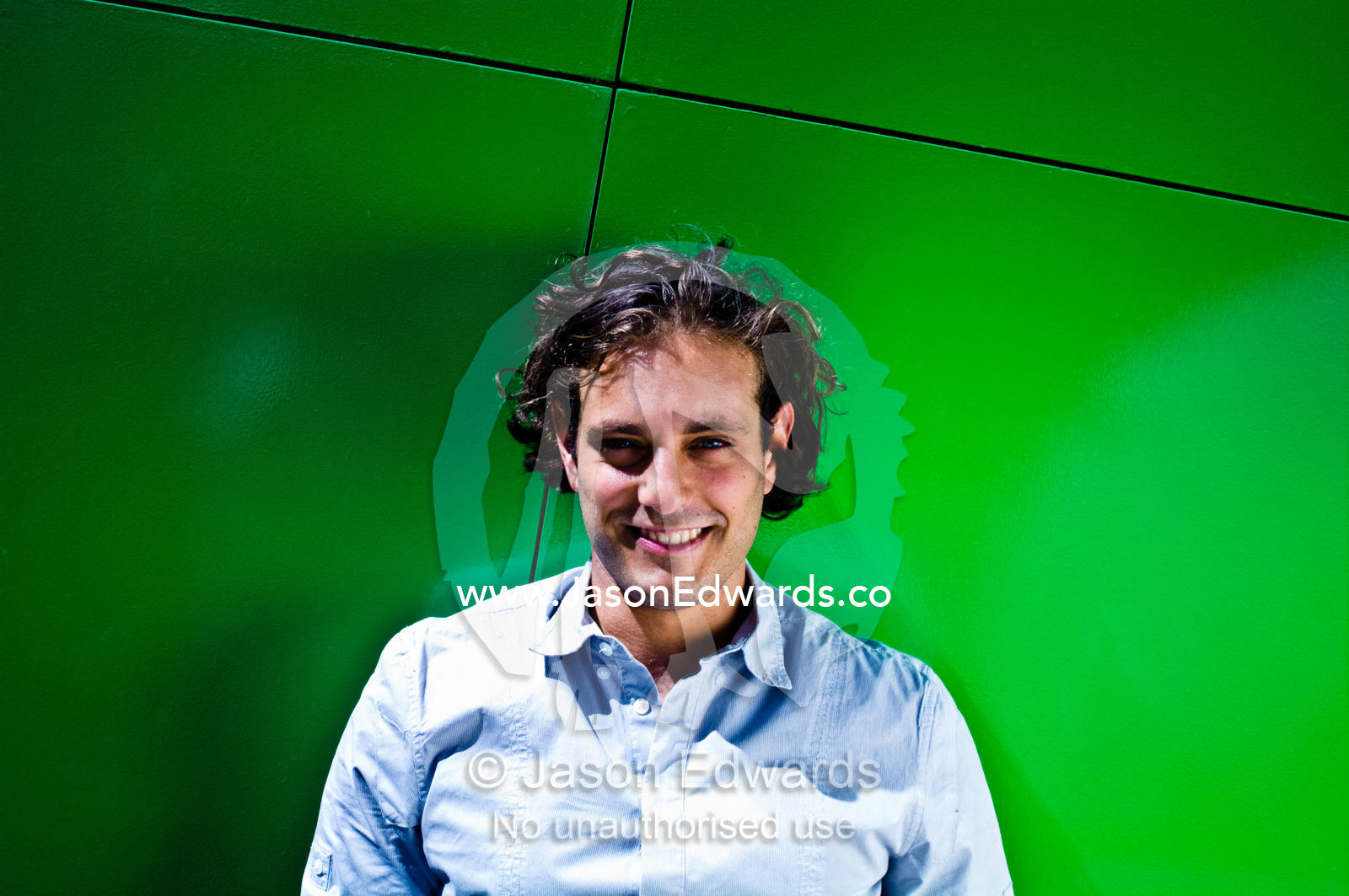 An attractive young man against a bright green architectural wall. Carlton, Melbourne, Victoria, Australia.