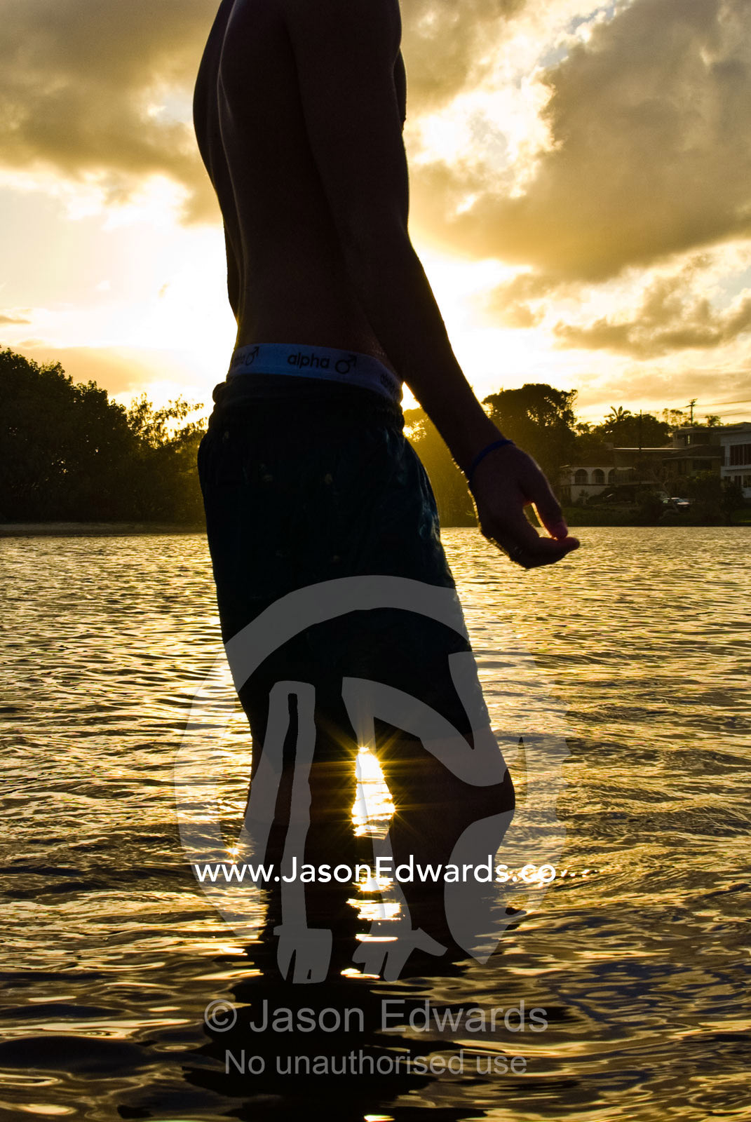 A teenage boy standing in the golden shallows at the beach at sunset. Moffat Beach, Caloundra, Sunshine Coast, Queensland, Australia.