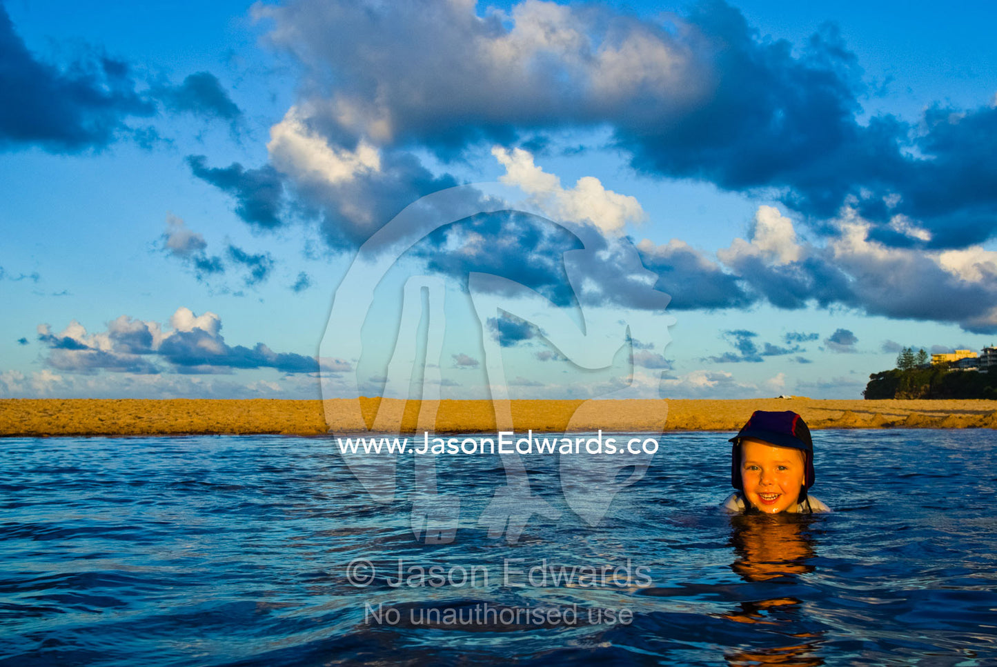 A young boy floating in the warm shallows at the beach at sunset. Moffat Beach, Caloundra, Sunshine Coast, Queensland, Australia.