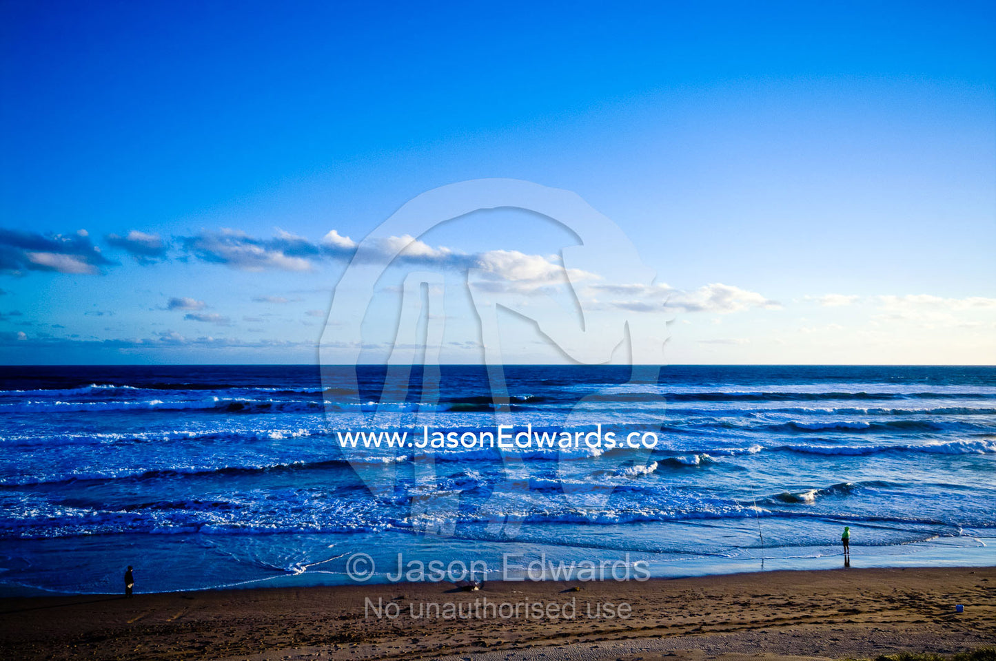 Men surf fishing on a wide beach at sunset as foamy waves tumble in. Venus Bay, Bass Strait, South Gippsland, Victoria, Australia.