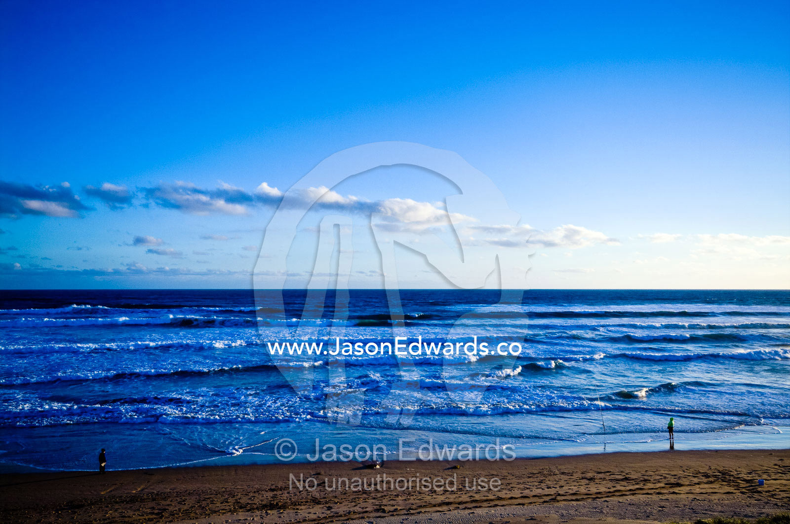 Men surf fishing on a wide beach at sunset as foamy waves tumble in. Venus Bay, Bass Strait, South Gippsland, Victoria, Australia.