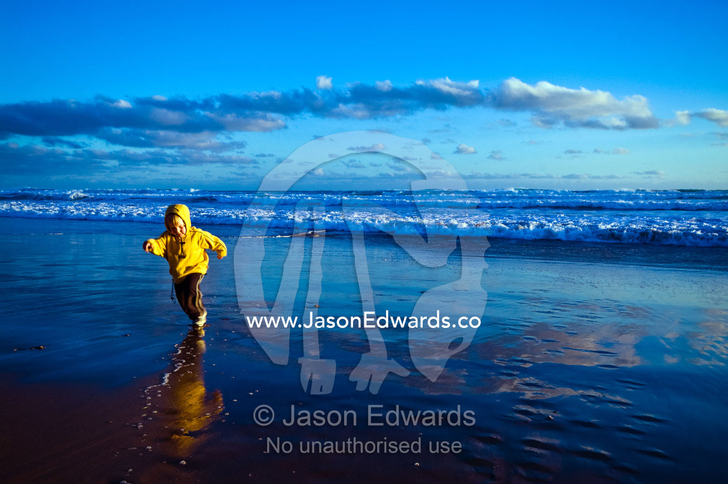 An excited young boy runs from approaching waves on a beach at sunset. Venus Bay, Bass Strait, South Gippsland, Victoria, Australia.
