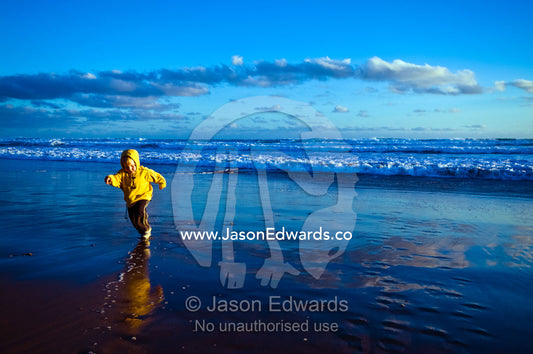 An excited young boy runs from approaching waves on a beach at sunset. Venus Bay, Bass Strait, South Gippsland, Victoria, Australia.