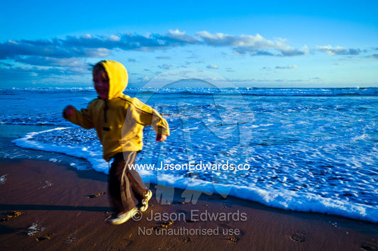 An excited young boy runs from approaching waves on a beach at sunset. Venus Bay, Bass Strait, South Gippsland, Victoria, Australia.