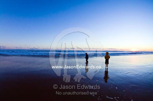 Two young friends jump and play on a wide beach at low tide at sunset. Venus Bay, Bass Strait, South Gippsland, Victoria, Australia.