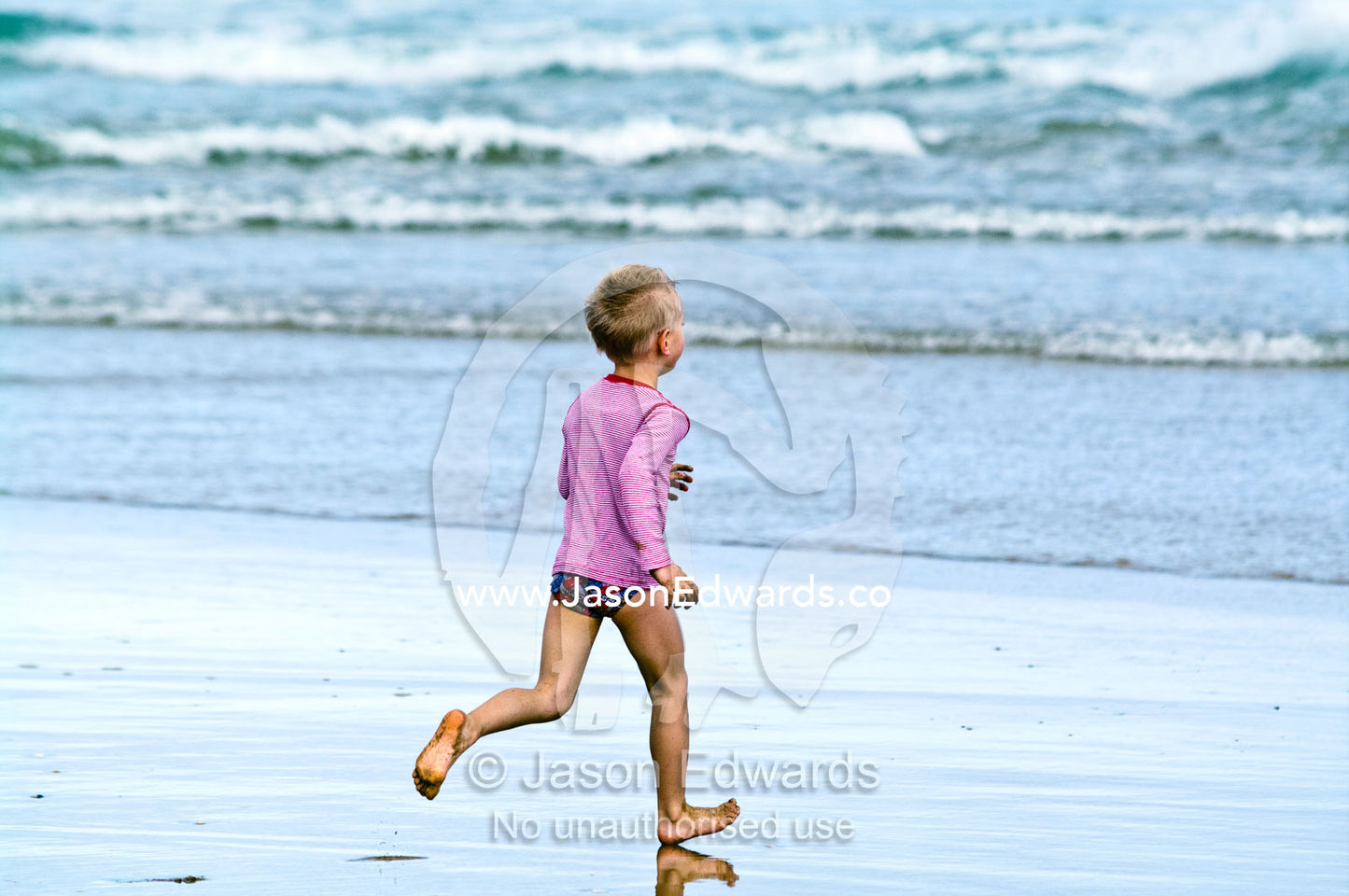 A fit and energetic blonde boy runs into the waves at the beach. Venus Bay, Bass Strait, South Gippsland, Victoria, Australia.