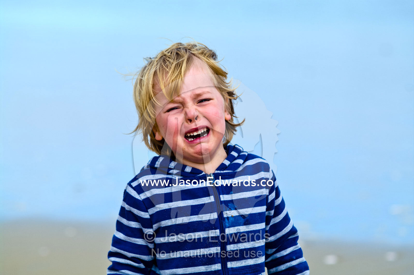 A young boy cries after hurting his foot on a rock at the beach. Venus Bay, Bass Strait, South Gippsland, Victoria, Australia.